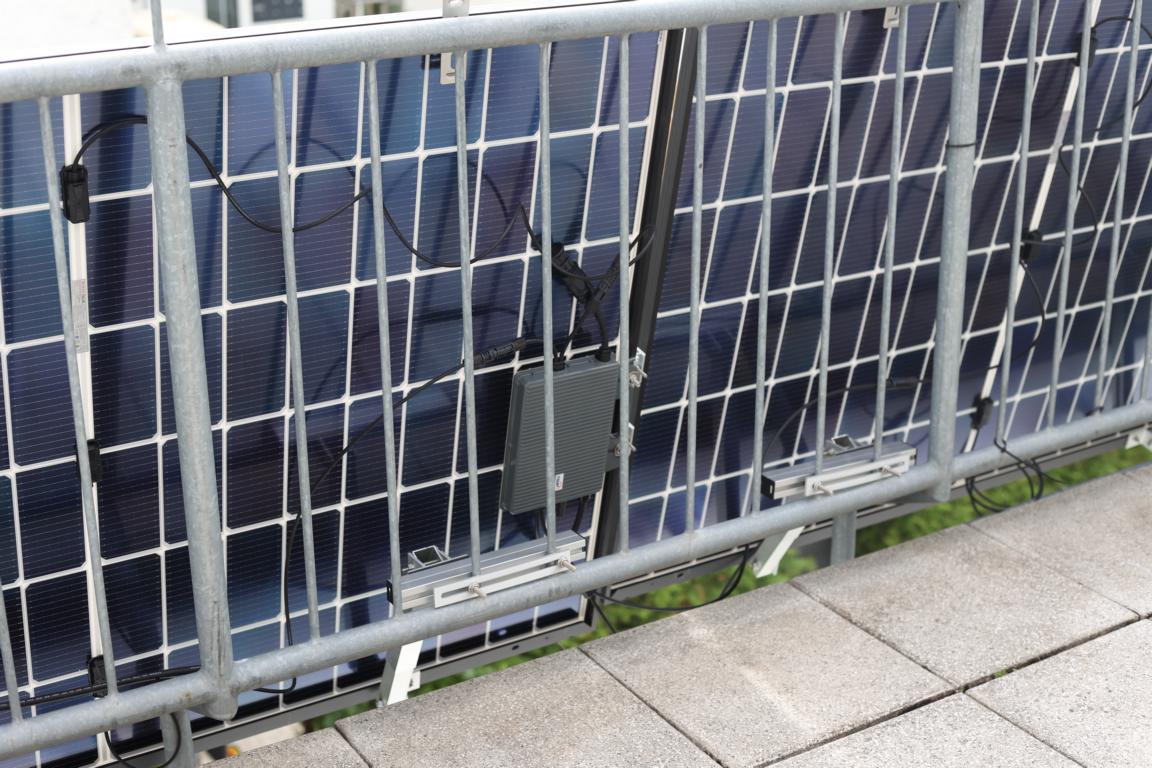TSUN M800 Wechselrichter hängt im Test an der Rückseite der Solarmodule an einem Balkongeländer.